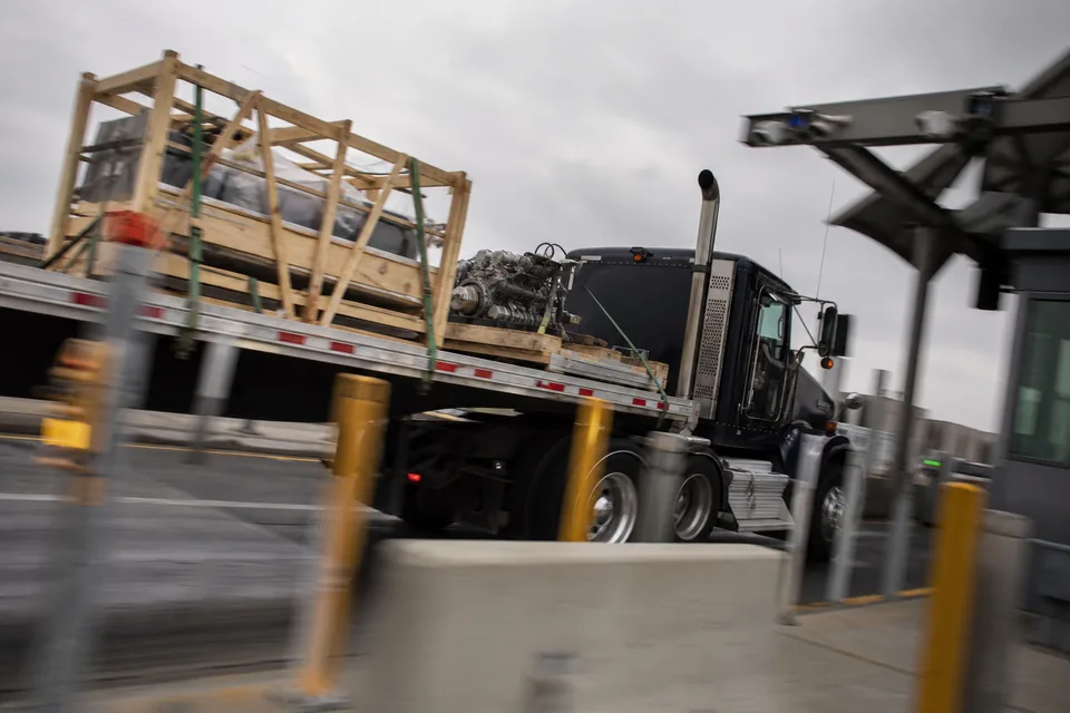Flatbed truck with crated machine parts moving through a cargo inspection gate